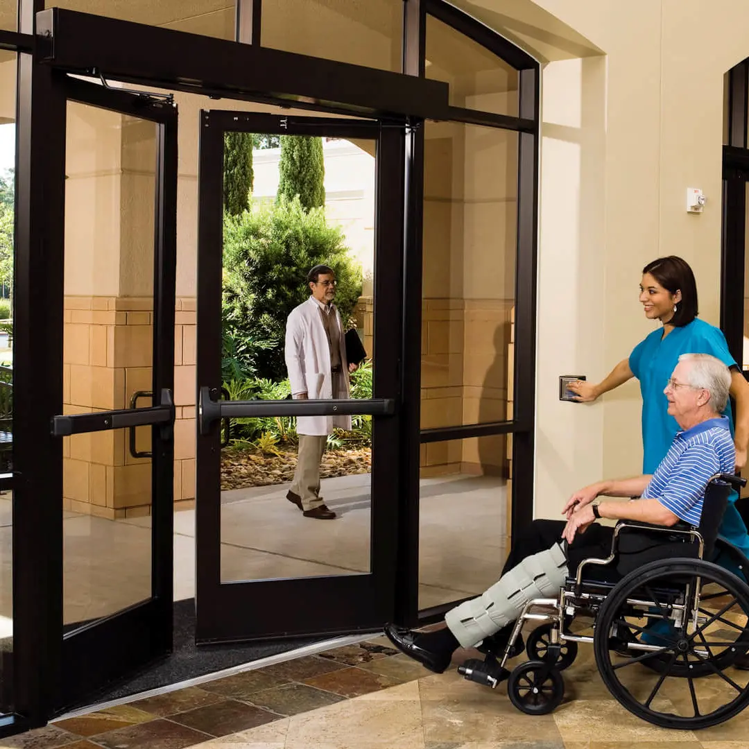 Puerta automática abatible con marco negro de aluminio y cristal claro.