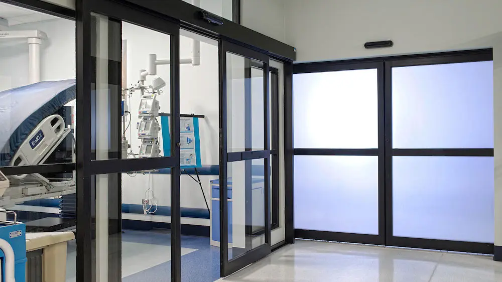 Puerta automática corrediza con marco negro de aluminio y cristal claro.